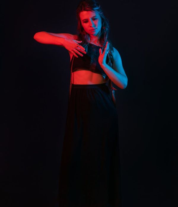 Woman performing a fluid, graceful cardio movement in a minimalist dark studio.